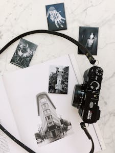 Artistic flat lay composition with a vintage camera, black-and-white photos on a marble background.